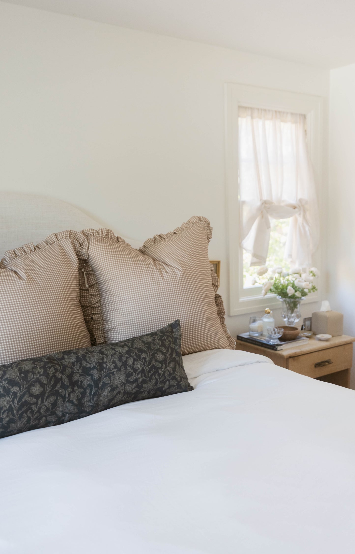 Tan and white mini gingham pillows with ruffled edges arranged on a bed.