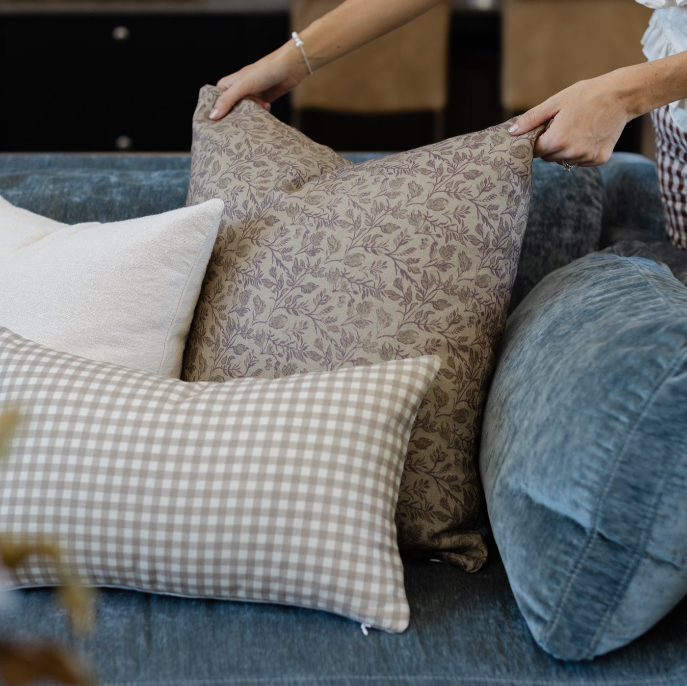 Faye pillow in taupe floral pattern displayed on blue upholstered sofa with checkered and solid pillows.