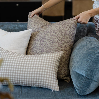 Faye pillow in taupe floral pattern displayed on blue upholstered sofa with checkered and solid pillows.