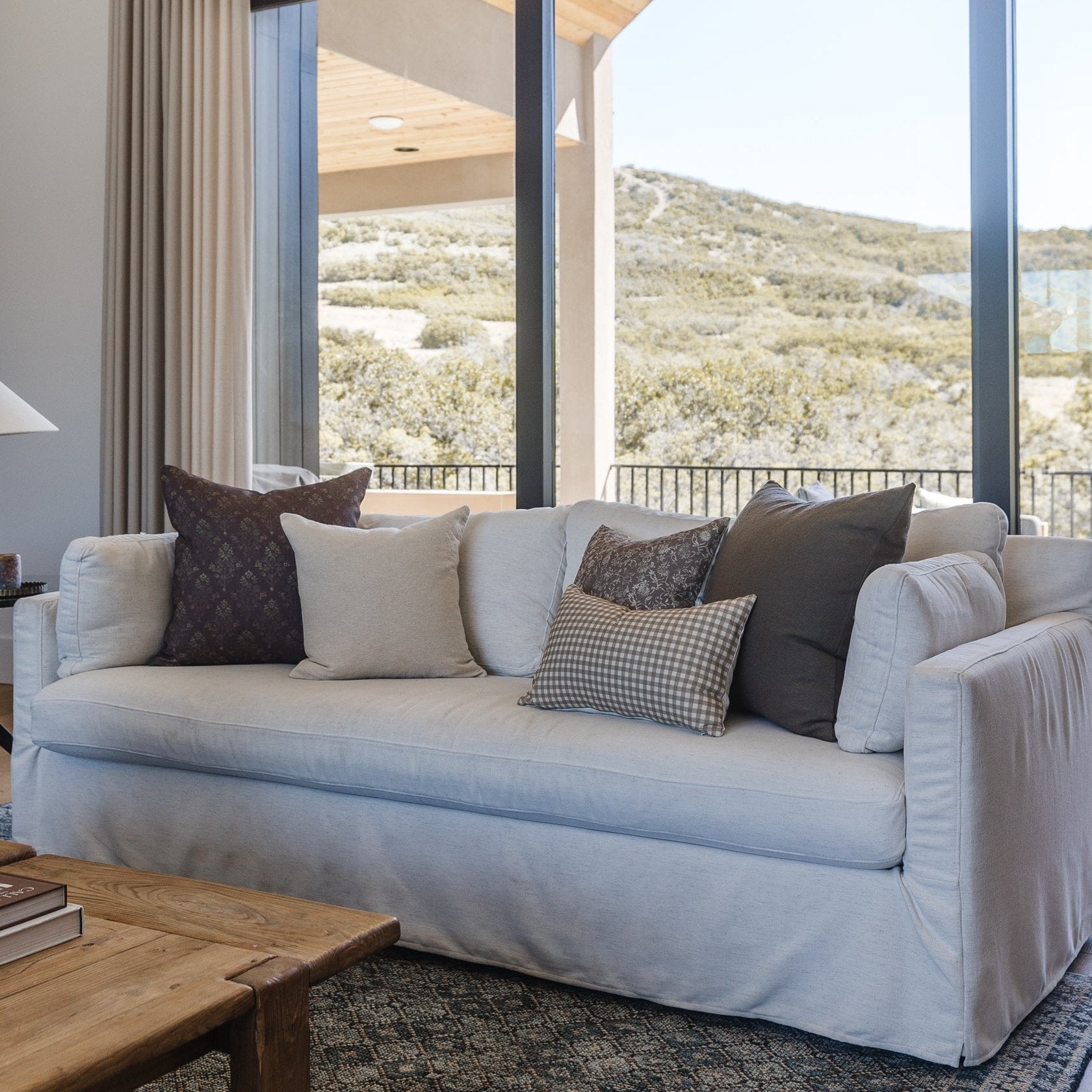 Tan and white gingham lumbar pillow on beige sofa with mountain view.