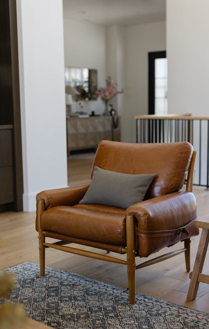 Olive green boucle lumbar pillow on cognac leather chair in modern living room setting.