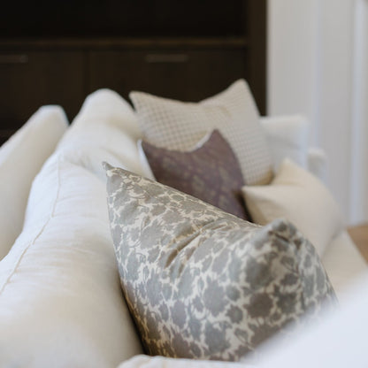 Gray damask patterned pillow arranged with white and cream textured pillows on a bed.