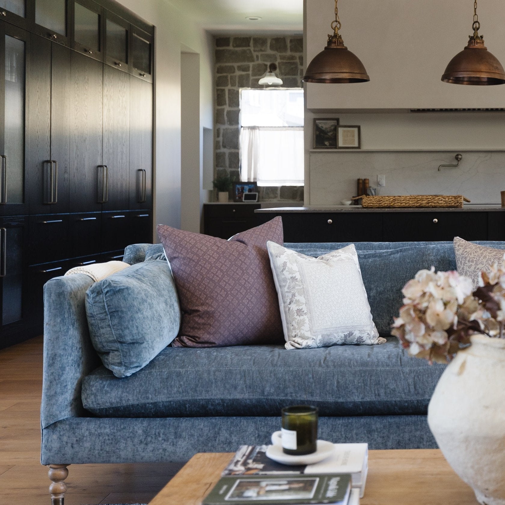 Gray corduroy sofa with rolled arms, decorative pillows, and turned wooden legs in a modern kitchen setting.