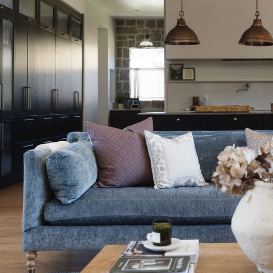 Gray corduroy sofa with rolled arms, decorative pillows, and turned wooden legs in a modern kitchen setting.