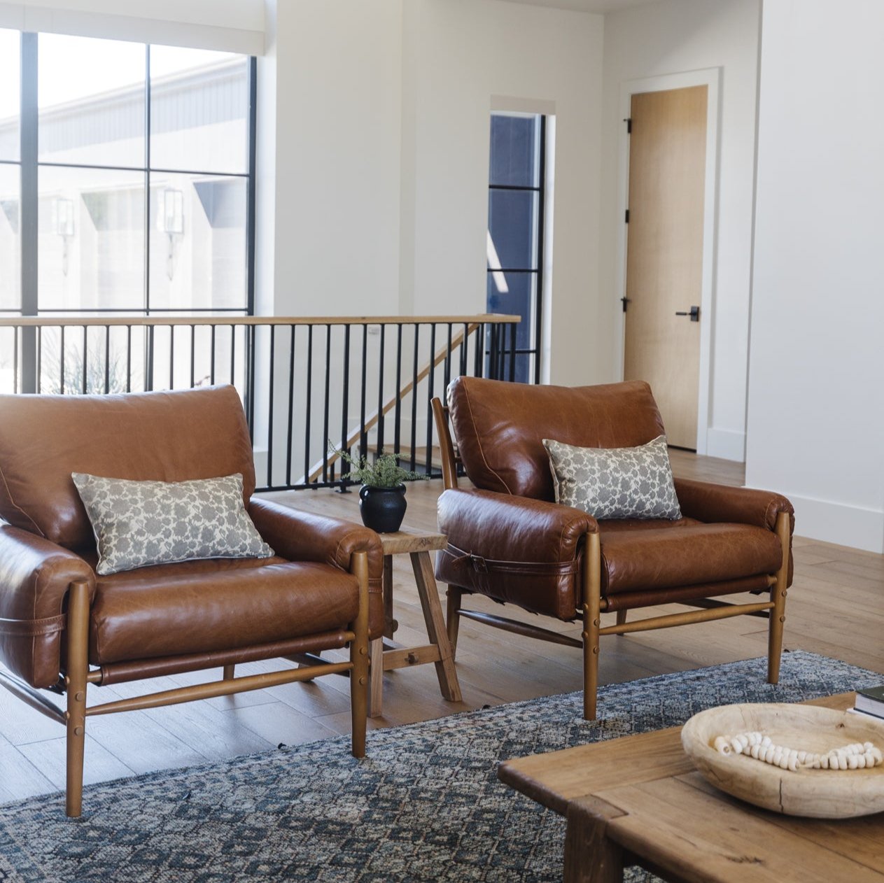 Beige geometric patterned lumbar pillow displayed on brown leather chair in living room setting.