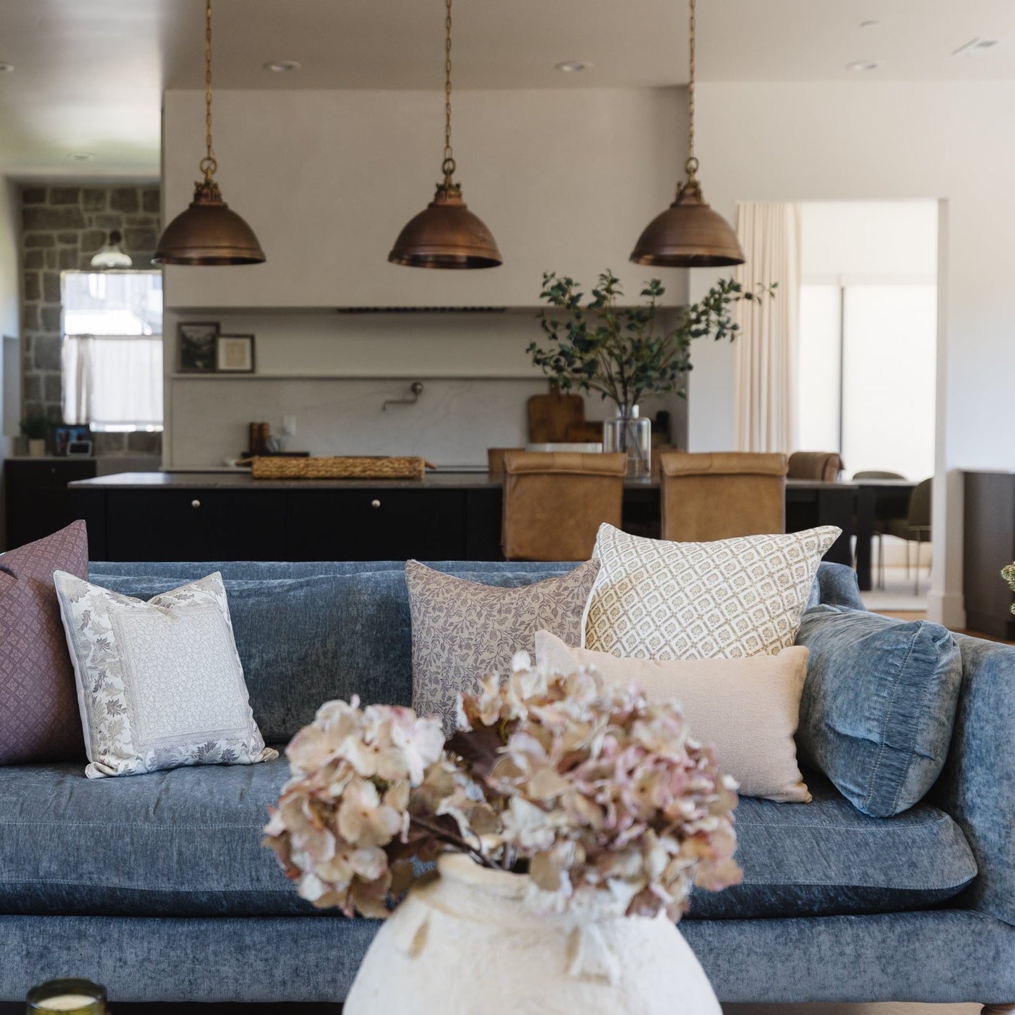 Blue linen sofa with patterned and solid pillows in a modern living room with bronze pendant lights.