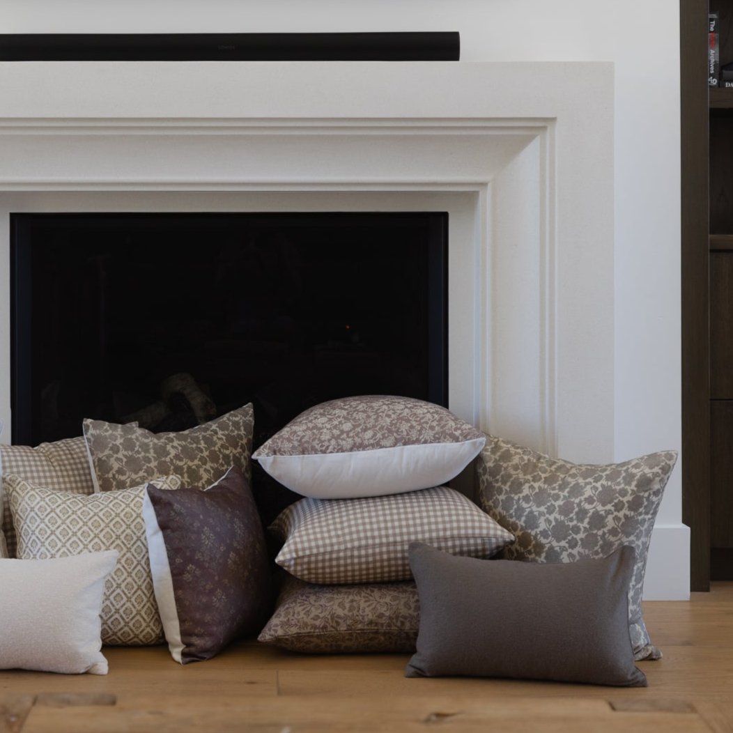 Tan and white gingham patterned pillow displayed among other decorative pillows in various patterns and colors.