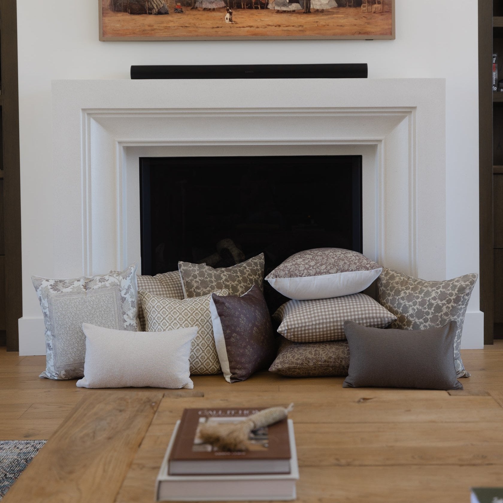 Collection of decorative pillows in neutral tones including patterned, solid, and textured designs arranged on wooden floor.