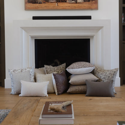 Collection of decorative pillows in neutral tones including patterned, solid, and textured designs arranged on wooden floor.