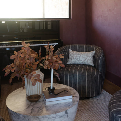 Burgundy wall with framed artwork above black piano, striped armchair with pillow, marble round table with dried flowers in v