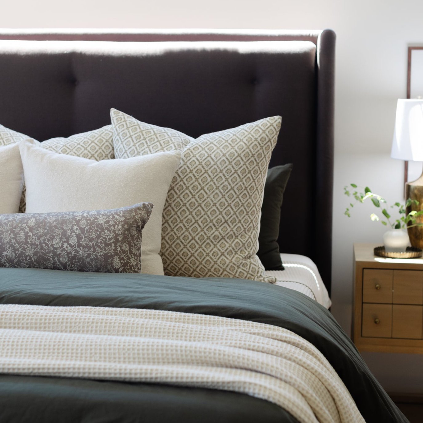 Cream and tan patterned linen pillows arranged on a dark upholstered bed with textured bedding.