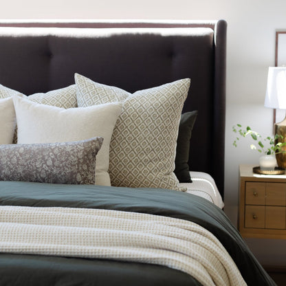 Cream and tan patterned linen pillows arranged on a dark upholstered bed with textured bedding.