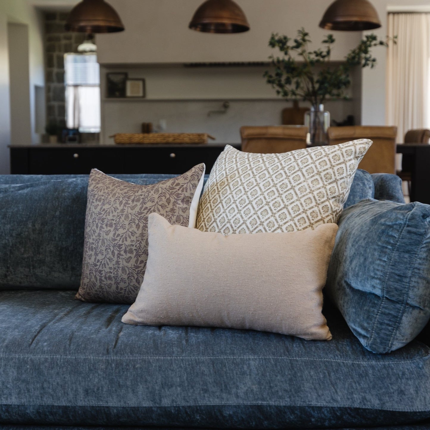 Blue upholstered sofa styled with decorative pillows in geometric and solid patterns in neutral tones.