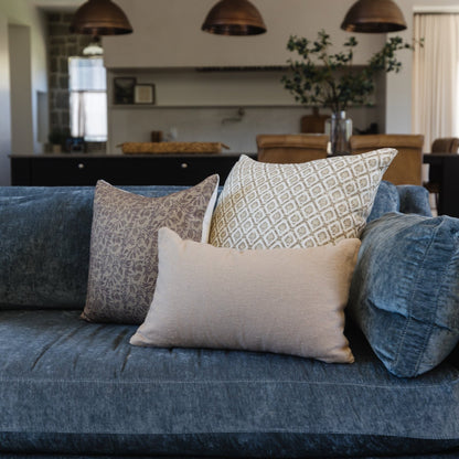 Blue upholstered sofa styled with decorative pillows in geometric and solid patterns in neutral tones.
