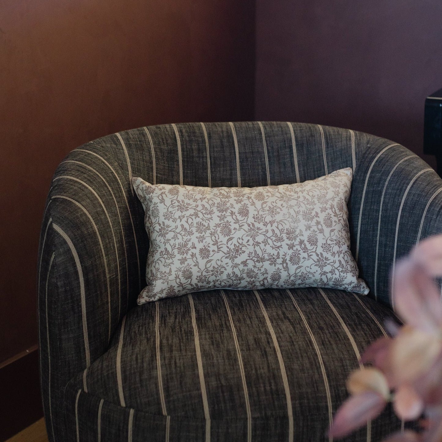 Rectangular lumbar pillow with beige floral damask pattern displayed on striped upholstered chair.