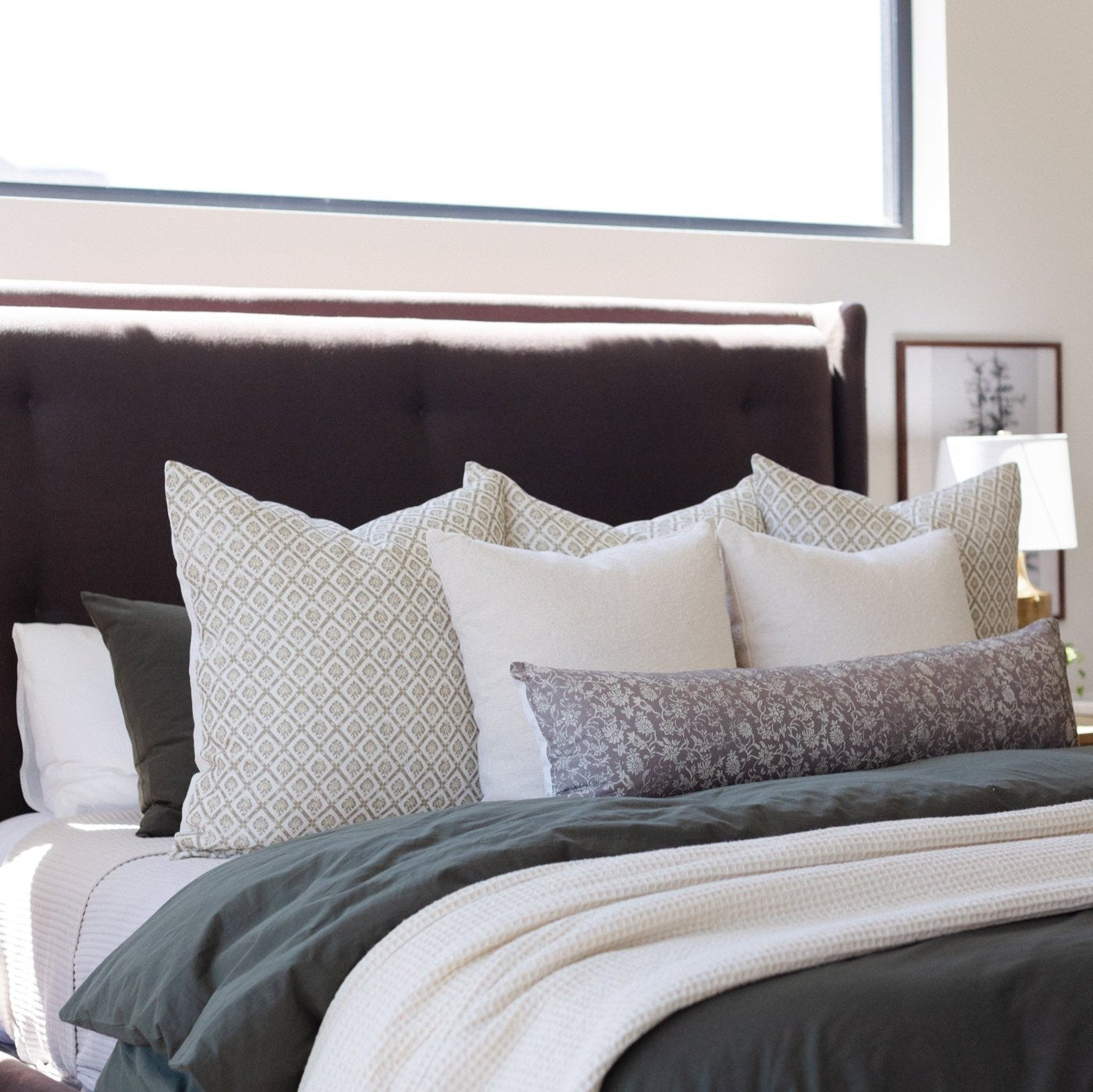 Ivory waffle-textured blanket layered on a bed with patterned and solid pillows.