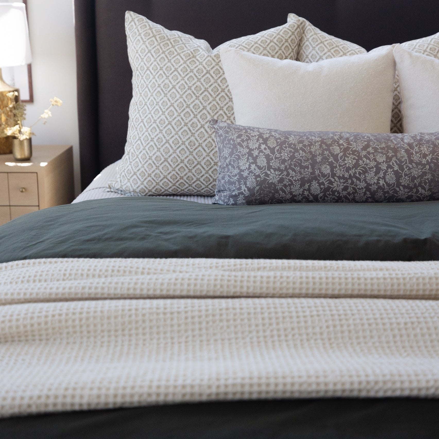 Ivory waffle-textured blanket draped over a bed with patterned pillows and dark bedding.