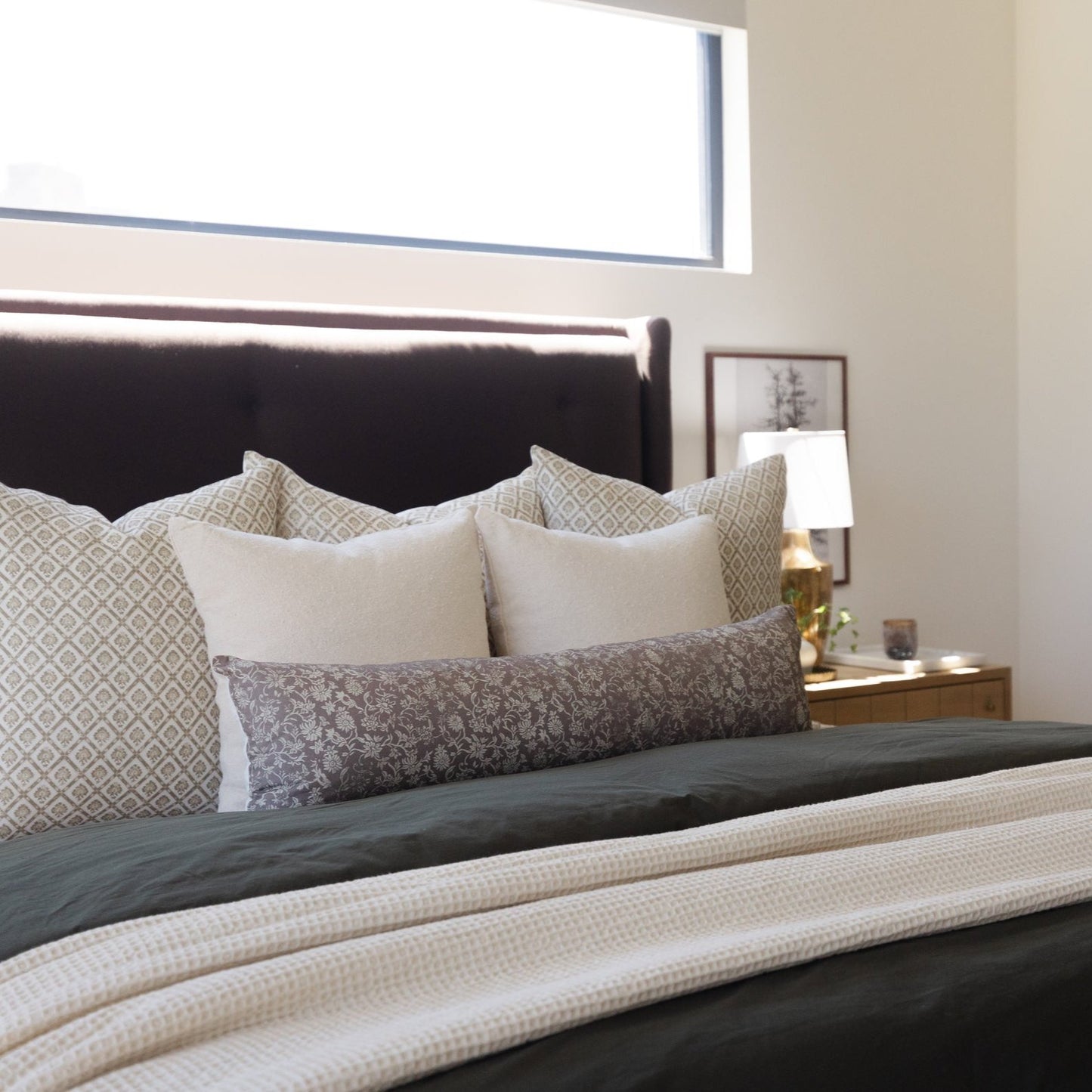 Beige and gray patterned linen pillows arranged on a black upholstered bed with matching bedding.