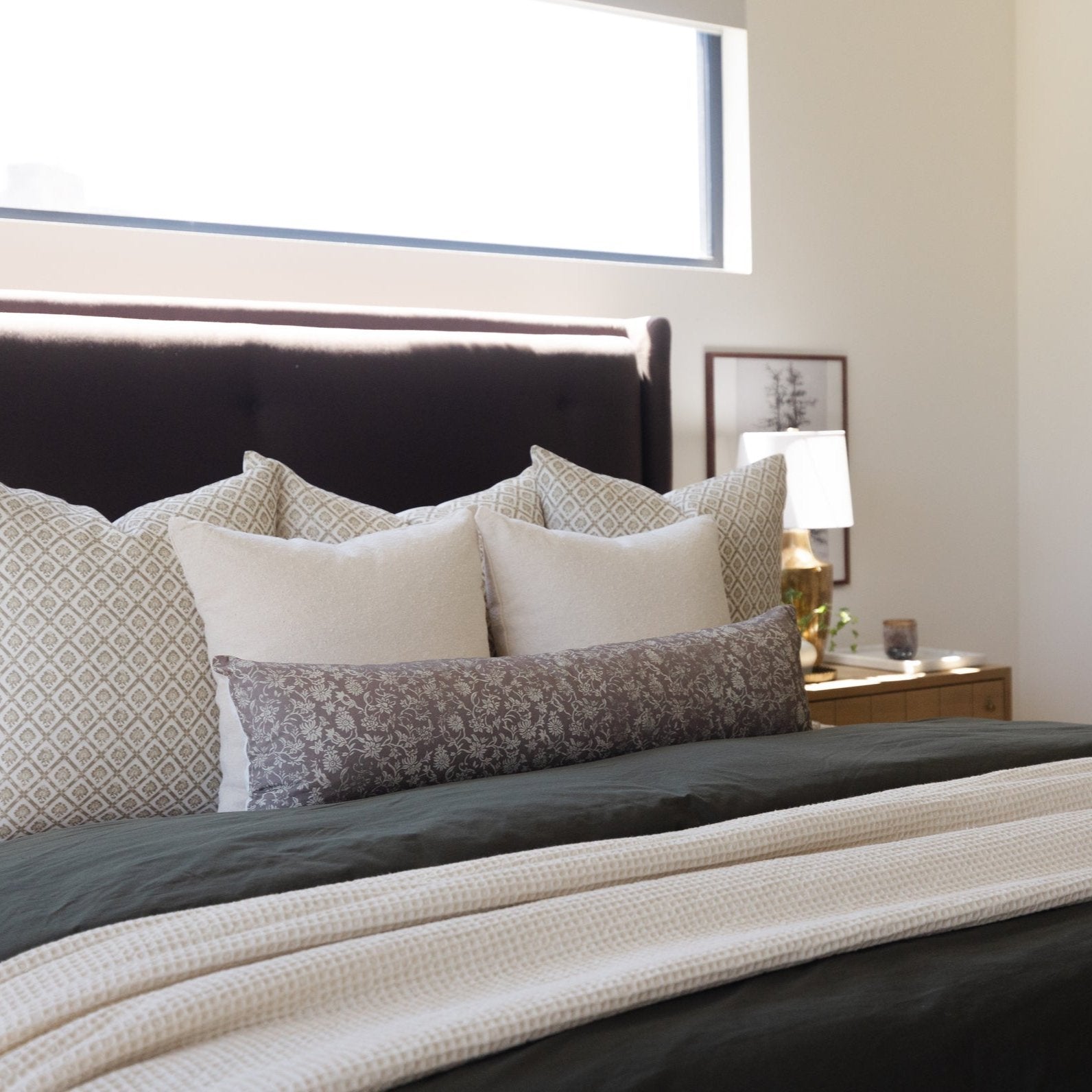 Beige and gray patterned linen pillows arranged on a black upholstered bed with matching bedding.