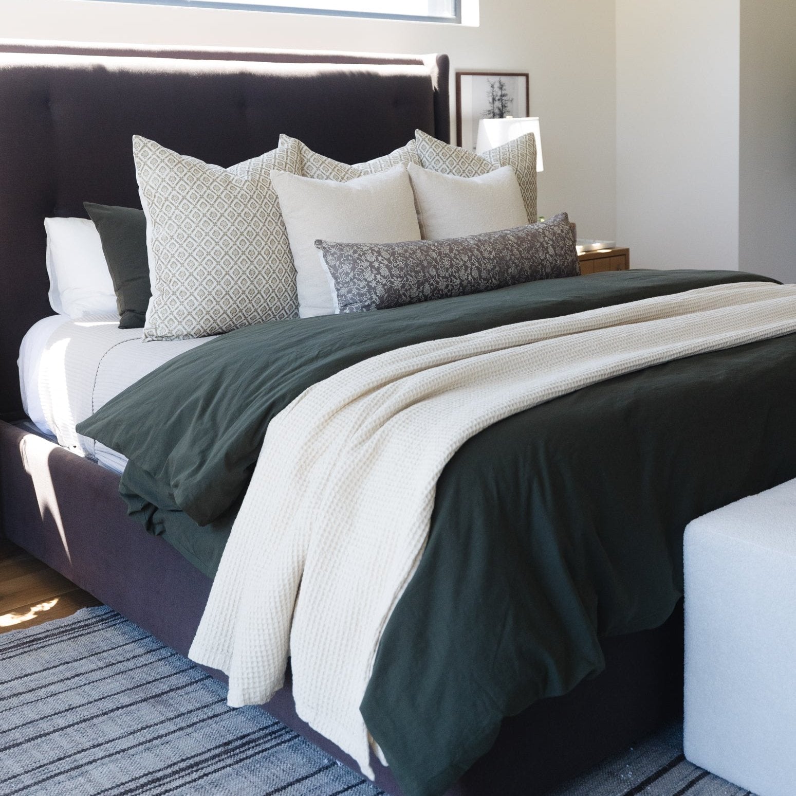 Ivory waffle-textured blanket draped across a bed with coordinating pillows and dark bedding.
