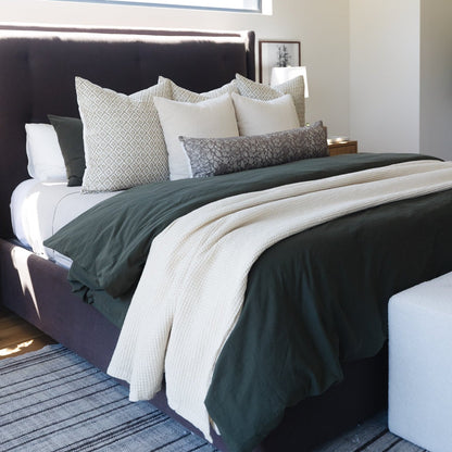 Ivory waffle-textured blanket draped across a bed with coordinating pillows and dark bedding.