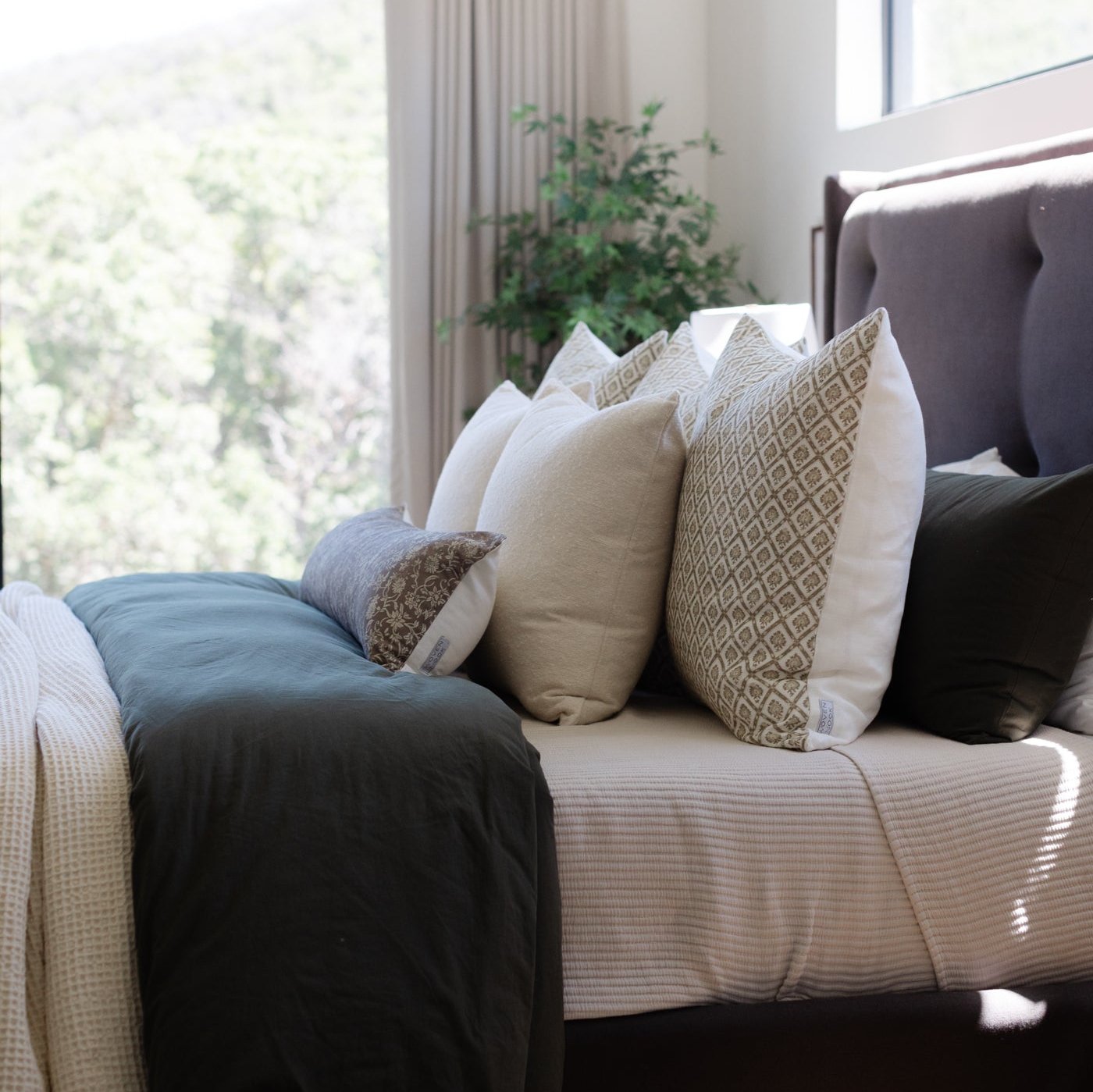Cream linen pillow arranged with other textured pillows on a bed with blue and black bedding.