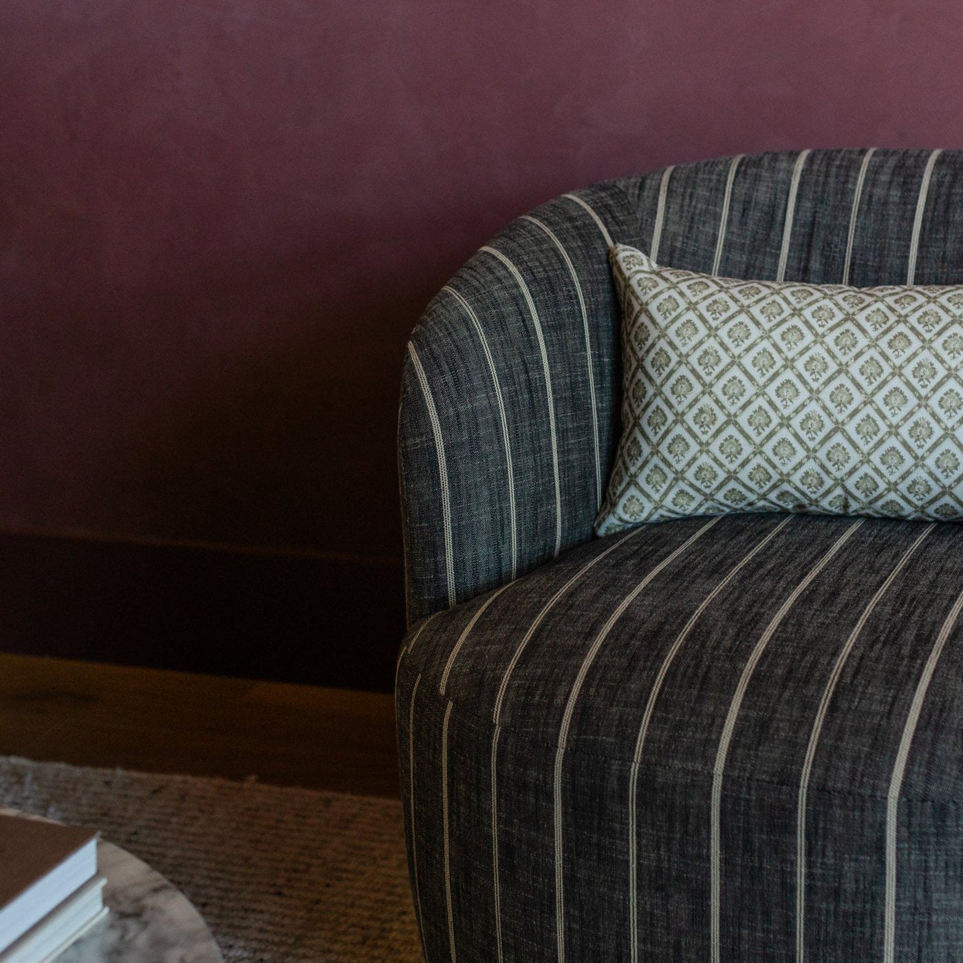 Cream linen lumbar pillow with geometric diamond pattern resting on striped gray armchair.