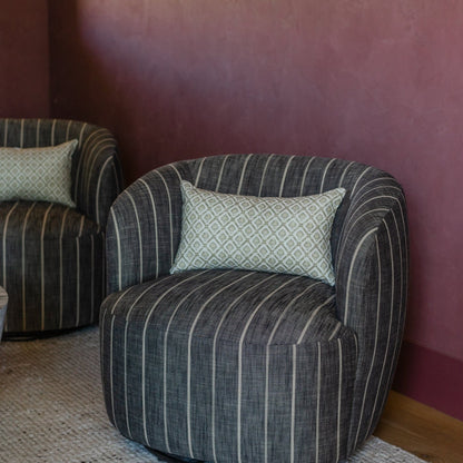 Cream linen lumbar pillow with geometric diamond pattern placed on striped gray armchair.