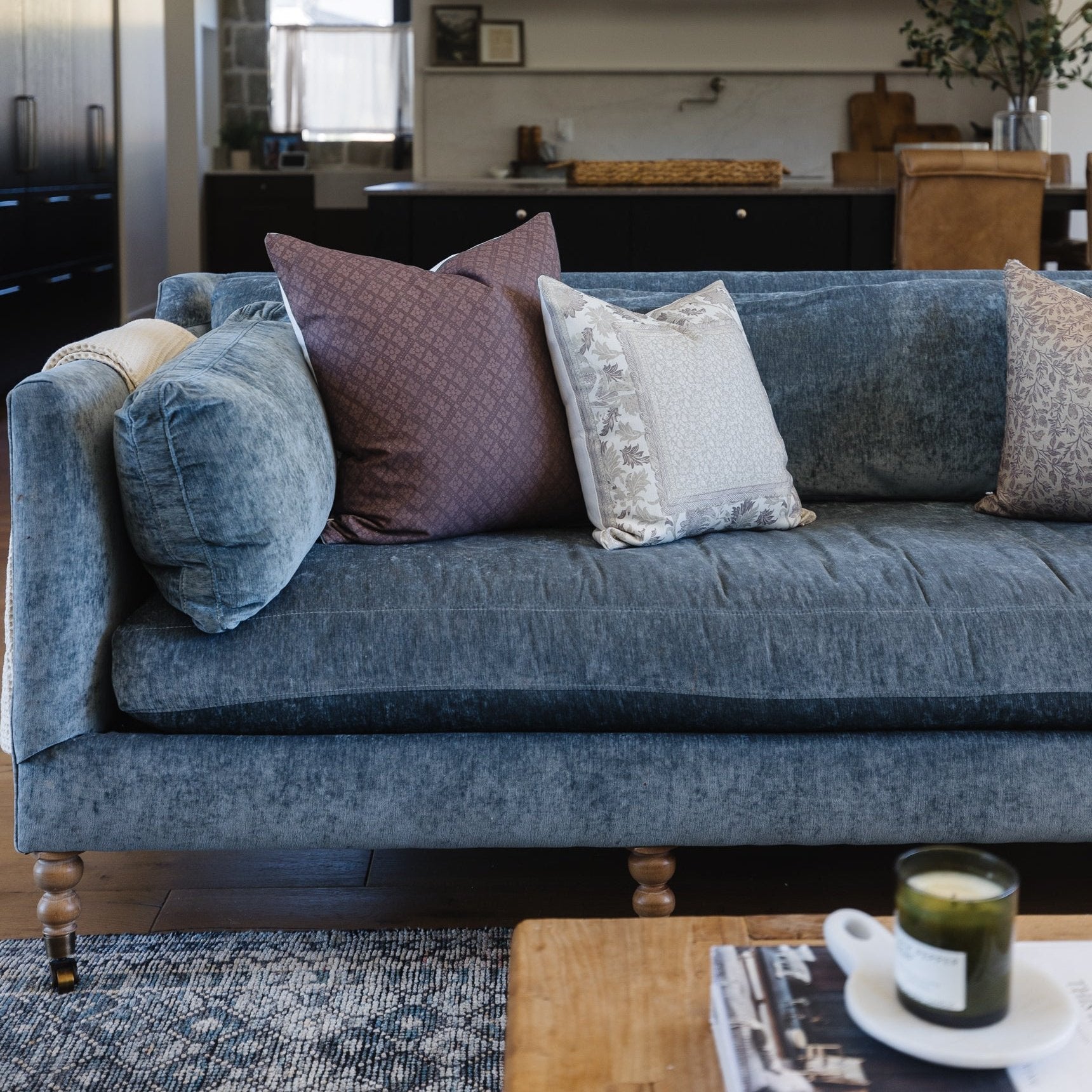 Maroon quilted throw pillow displayed on blue upholstered sofa with wooden legs in living room setting.