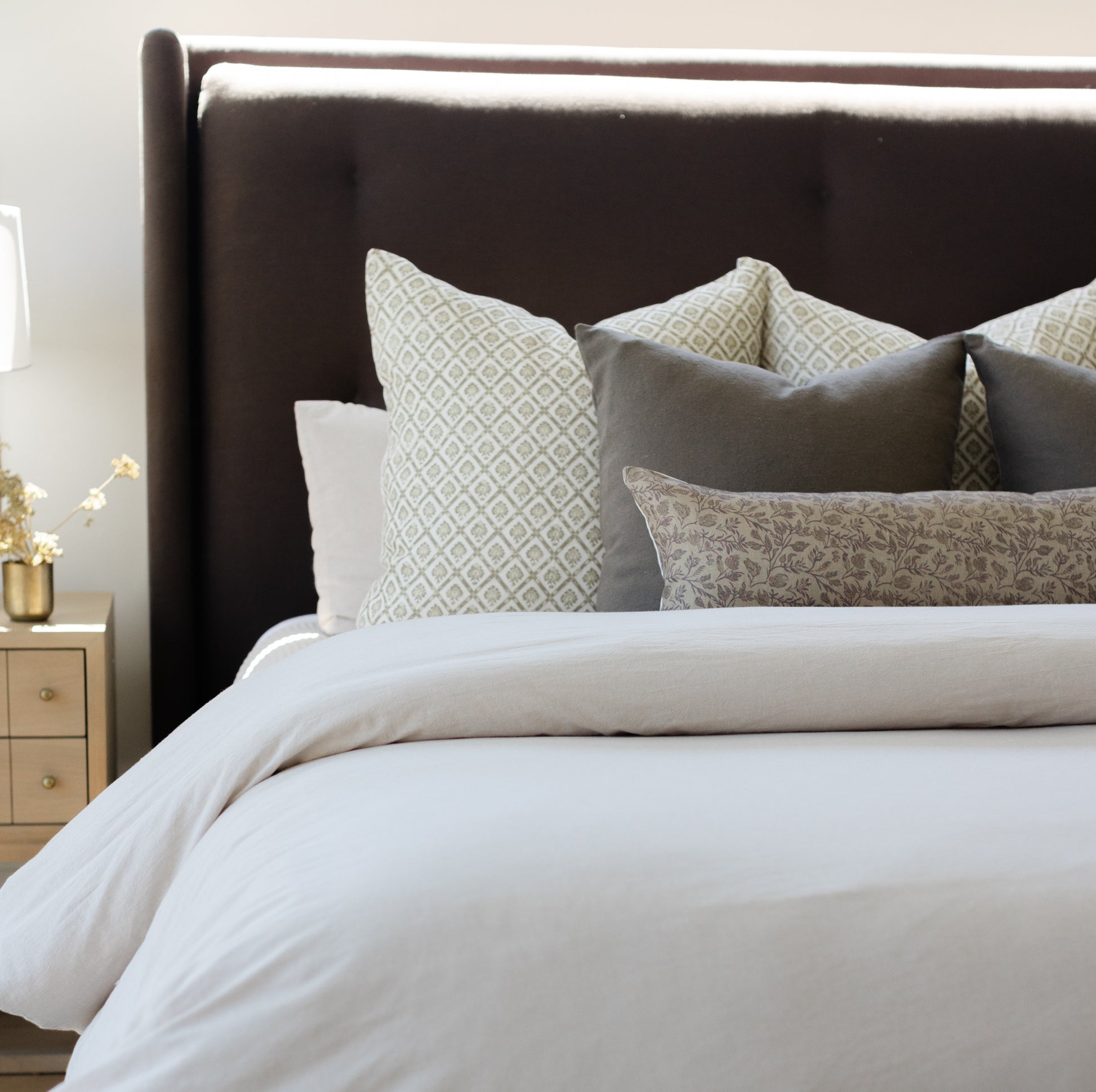 Bed with dark brown upholstered headboard, white bedding, and decorative pillows in geometric and floral patterns.