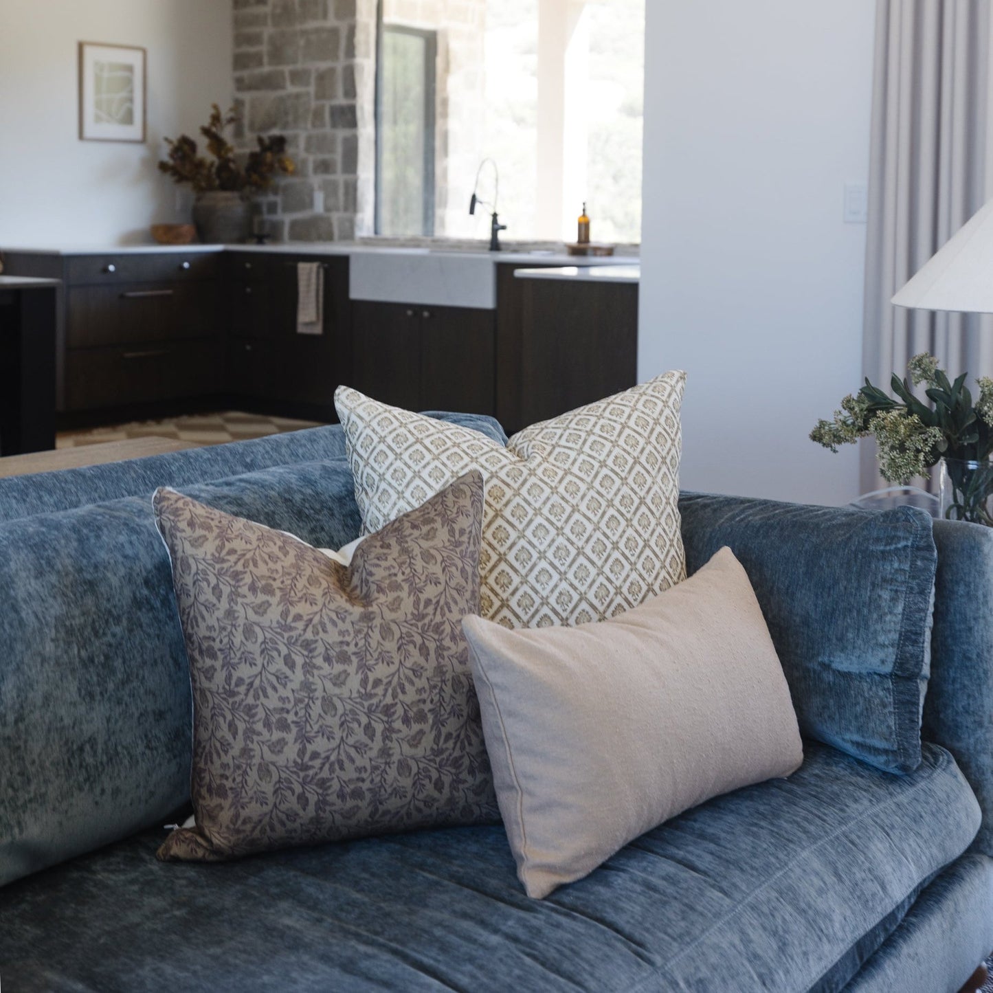 Three decorative pillows on a blue linen sofa with geometric and damask patterns in neutral tones.