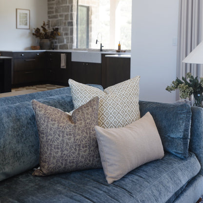 Three decorative pillows on a blue linen sofa with geometric and damask patterns in neutral tones.