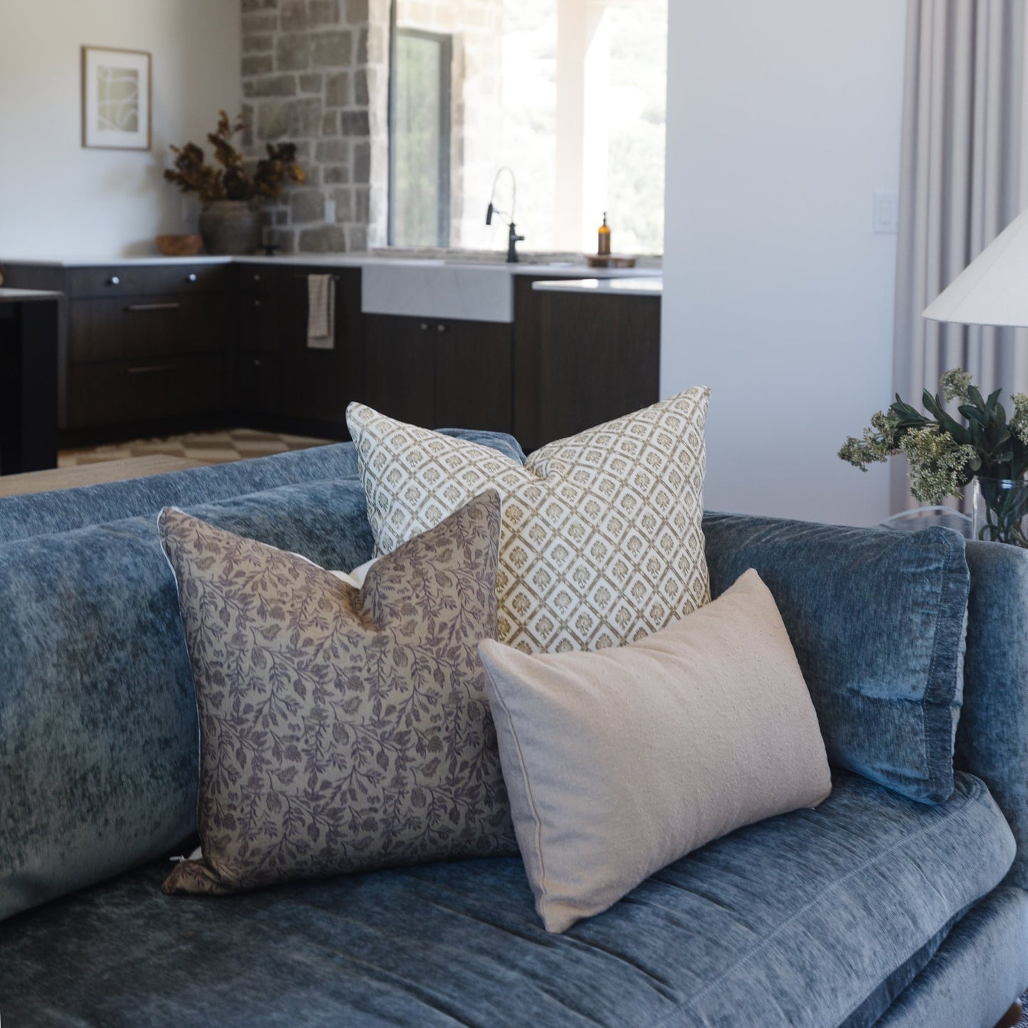 Three decorative pillows on a blue sofa: one with beige damask pattern, one with geometric diamond print, and one solid cream