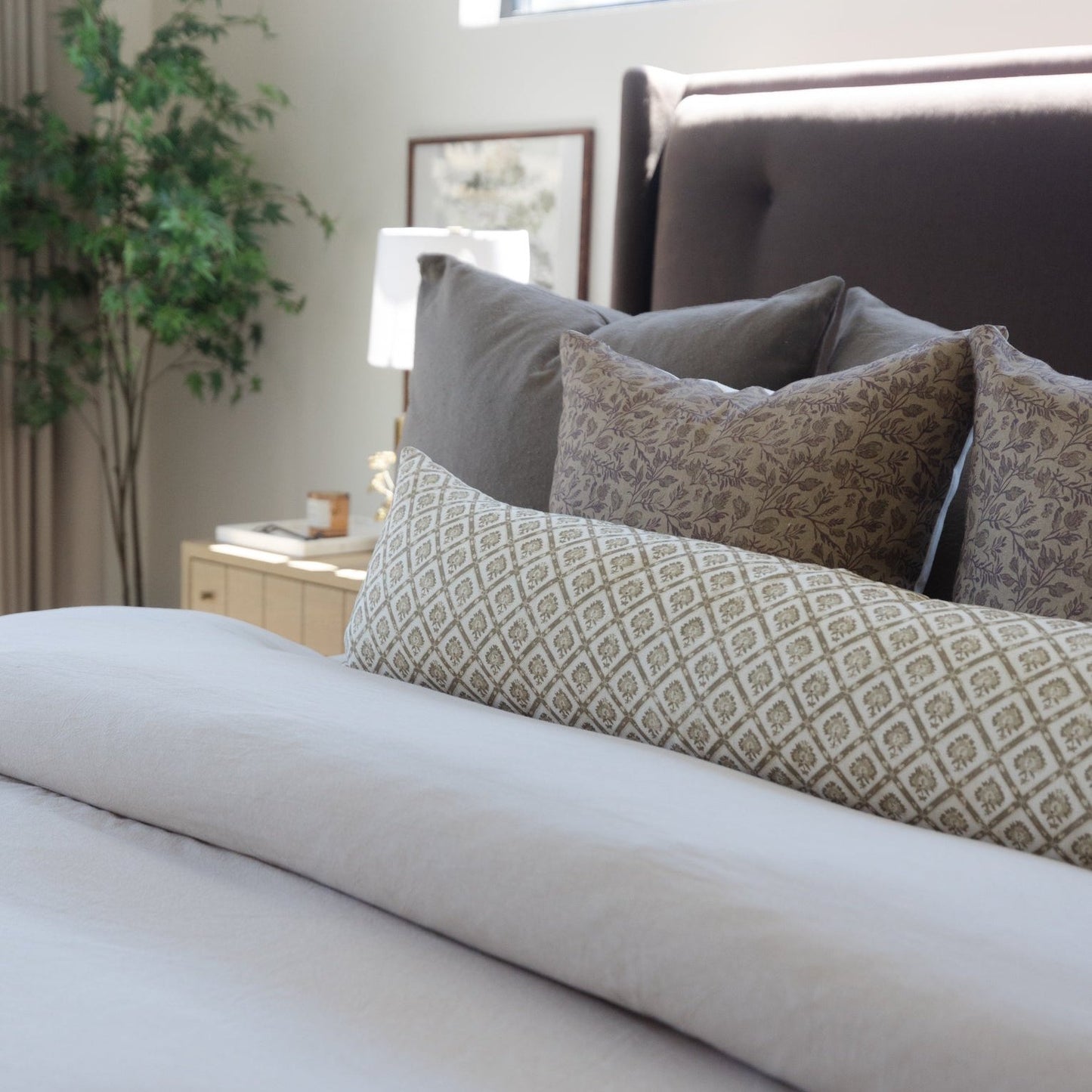 Beige linen lumbar pillow with geometric pattern displayed on bed with gray pillows and white bedding.