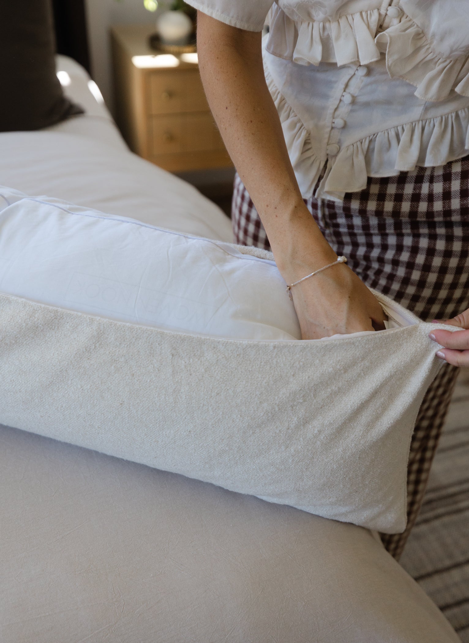 Off-white boucle lumbar pillow with textured weave and tucked corners displayed on a bed.