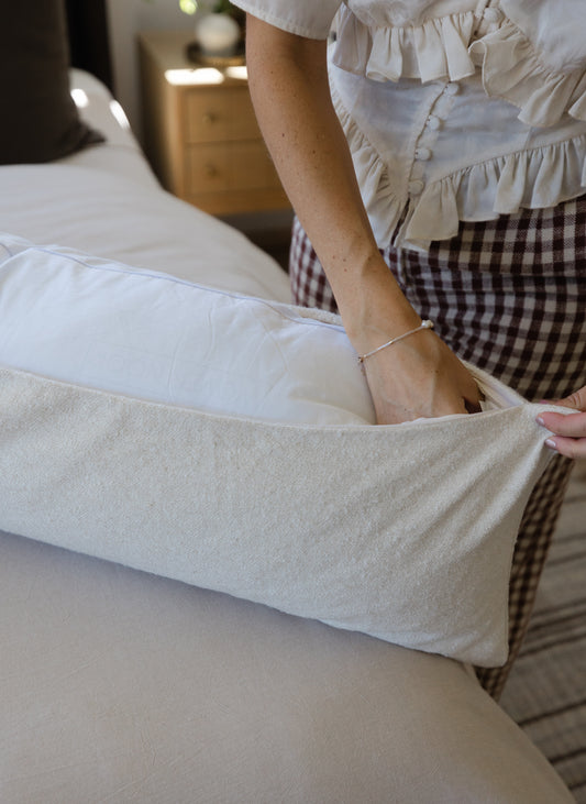 Off-white boucle lumbar pillow with textured weave and tucked corners displayed on a bed.