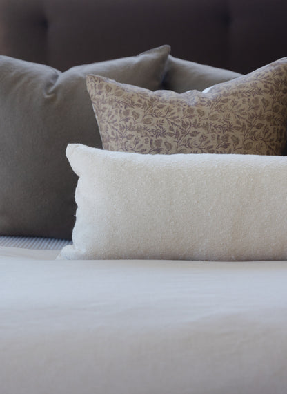 Off-white boucle lumbar pillow with textured weave displayed on bedding.