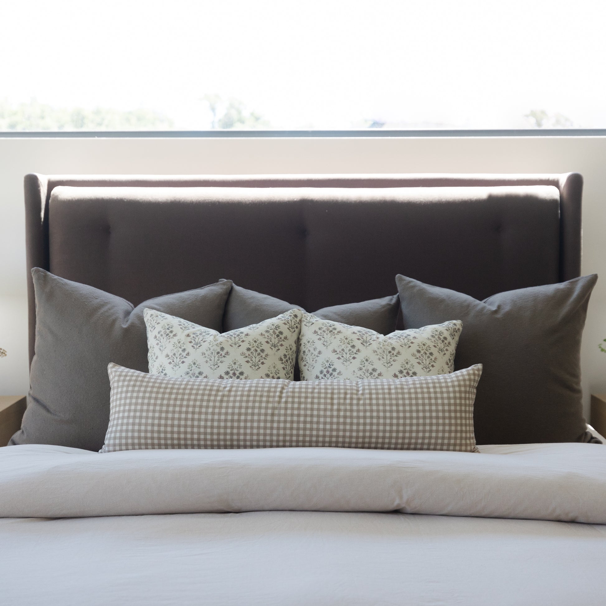 Charcoal gray upholstered bed headboard with decorative pillows in gray, patterned, and gingham fabrics.