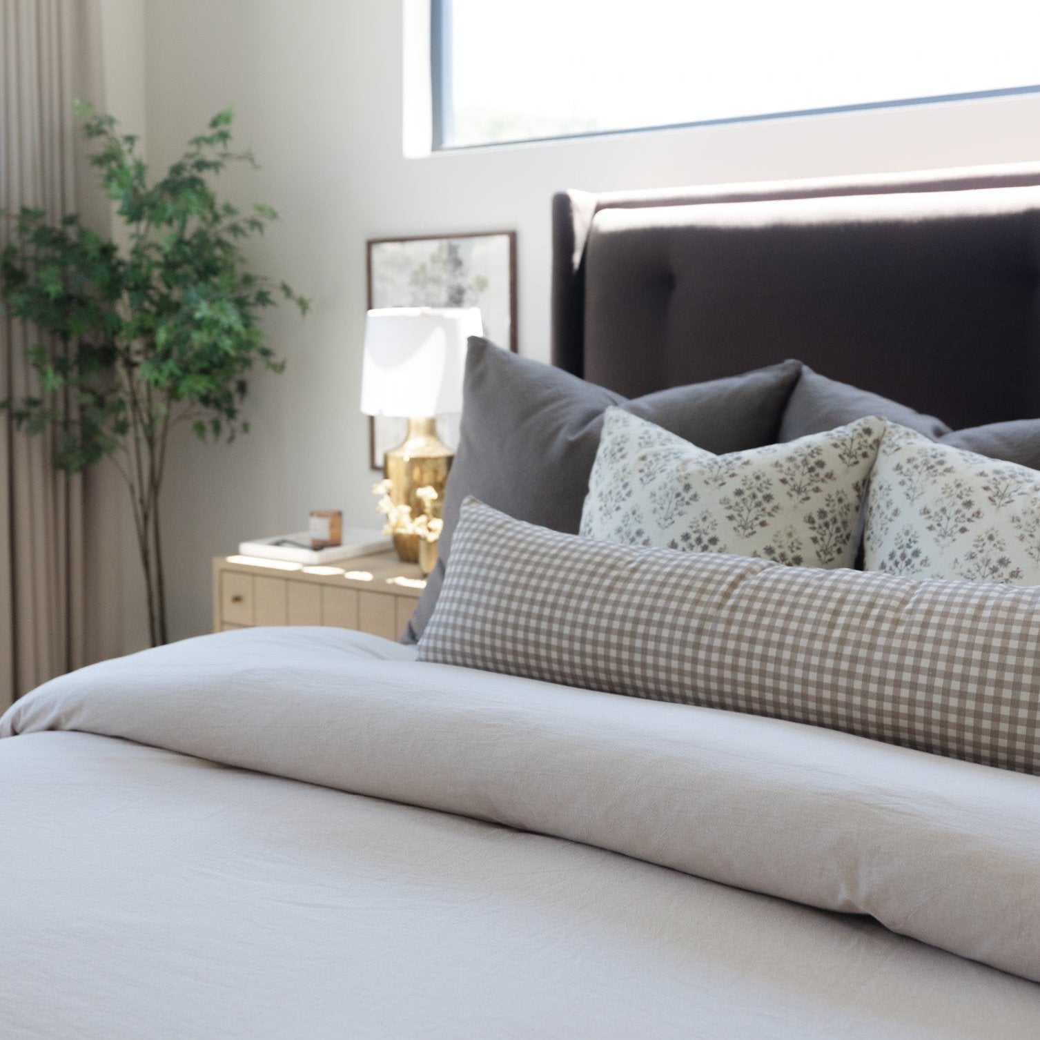 Tan and white gingham lumbar pillow displayed on a bed with gray pillows and white bedding.