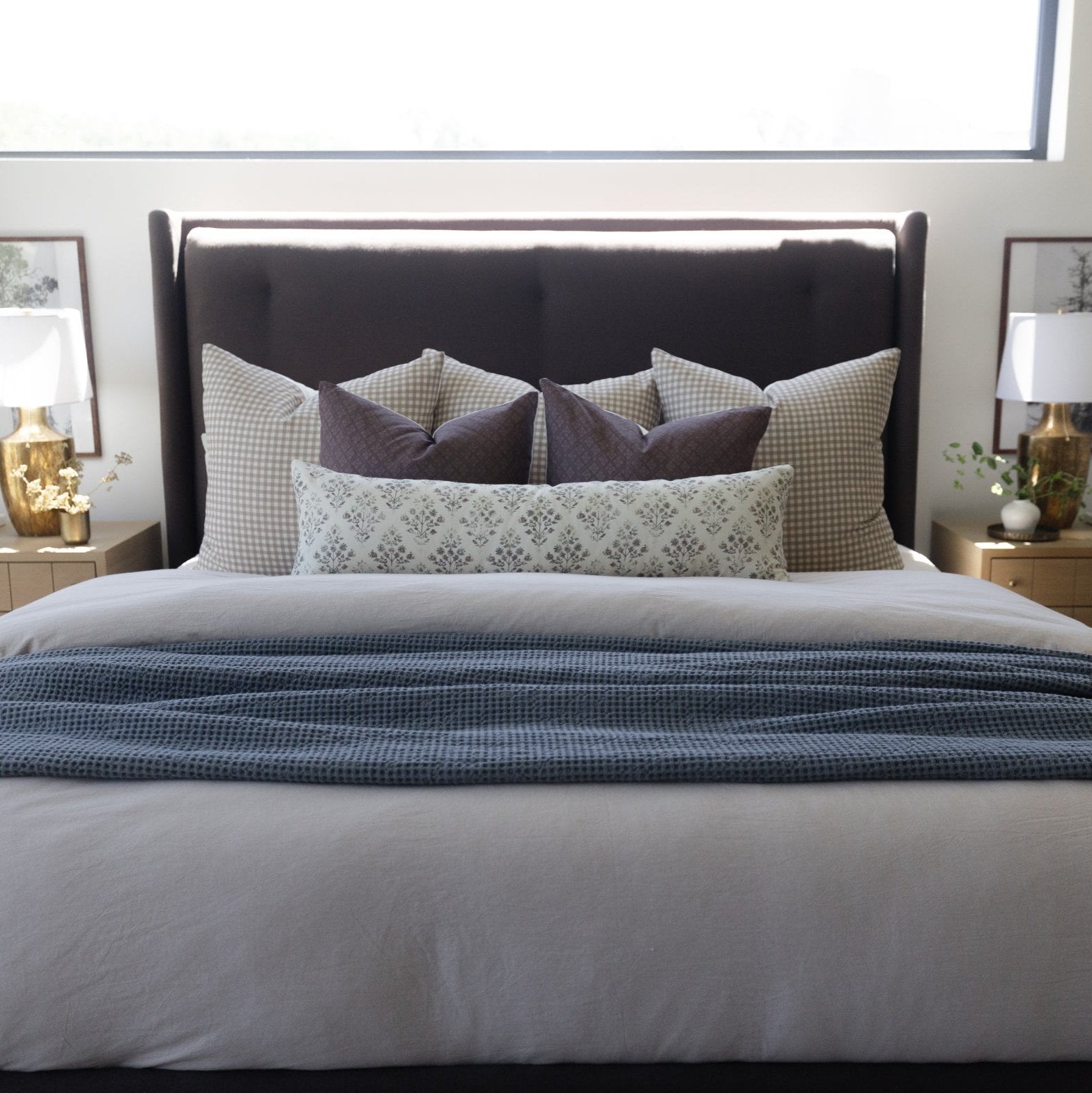 Lumbar pillow in cream with geometric pattern displayed among decorative pillows on a made bed.