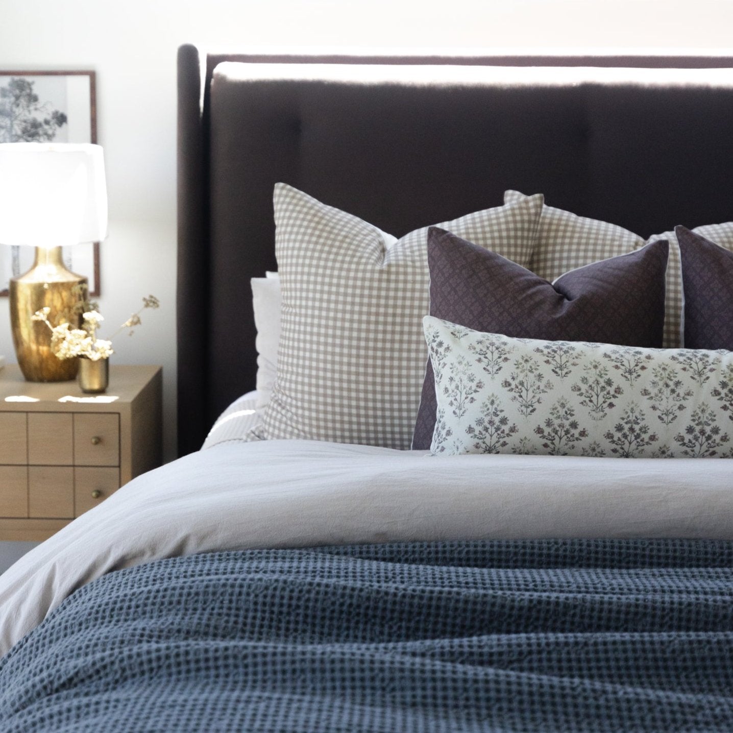 Gray and cream checkered lumbar pillow displayed on a made bed with patterned pillows and blue textured bedding.