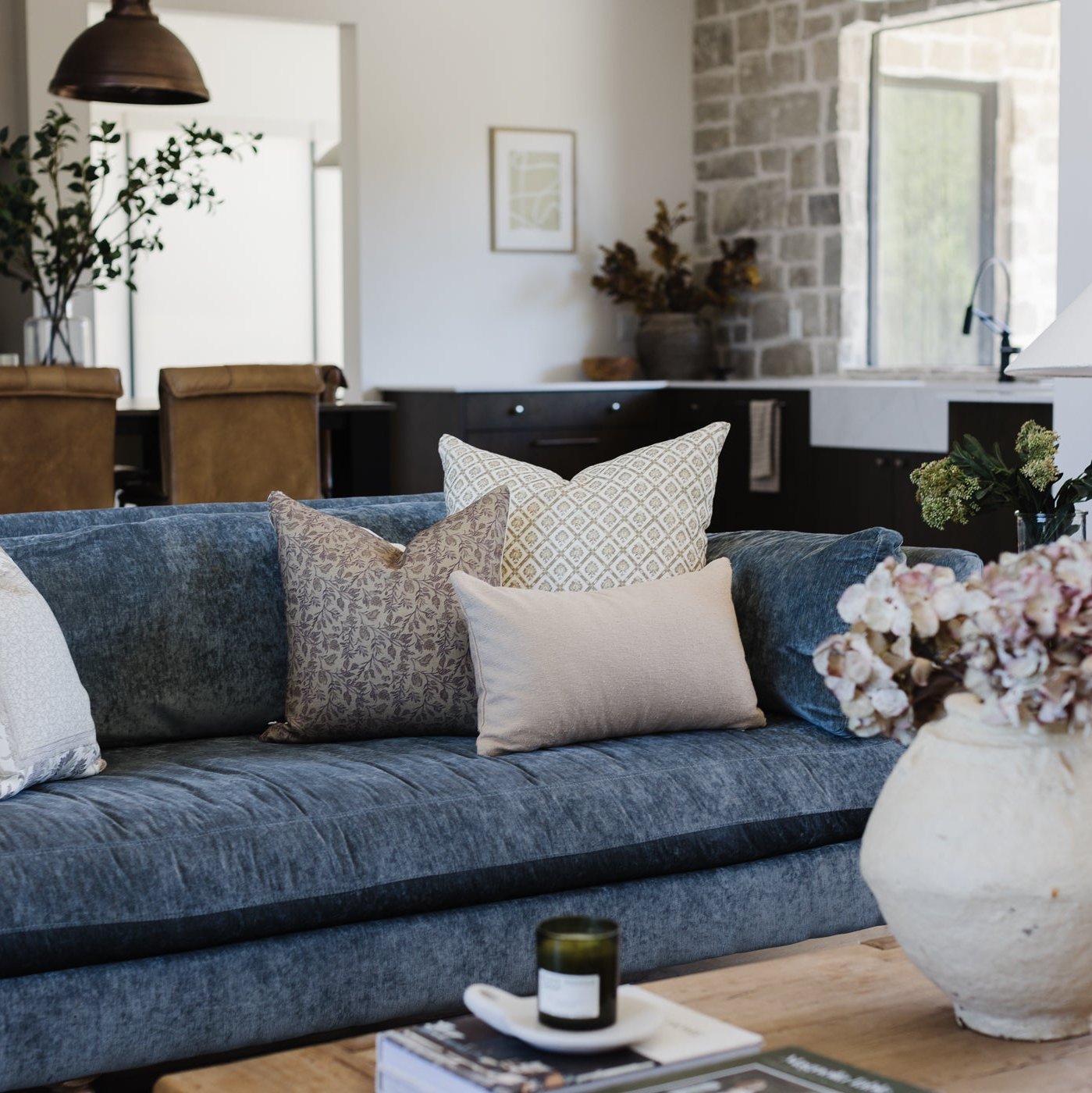 Blue linen sofa with decorative pillows in various patterns and neutral tones in a modern living room setting.