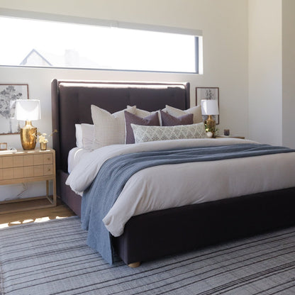 Afton lumbar pillow in light gray displayed on a bed with multiple decorative pillows and blue striped bedding.