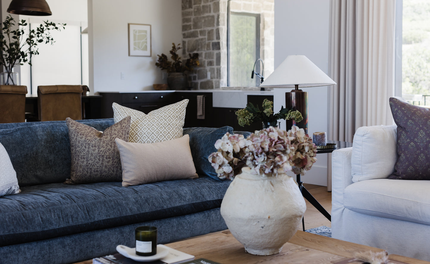 Beige boucle lumbar pillow displayed on dark blue sofa in modern living room setting.