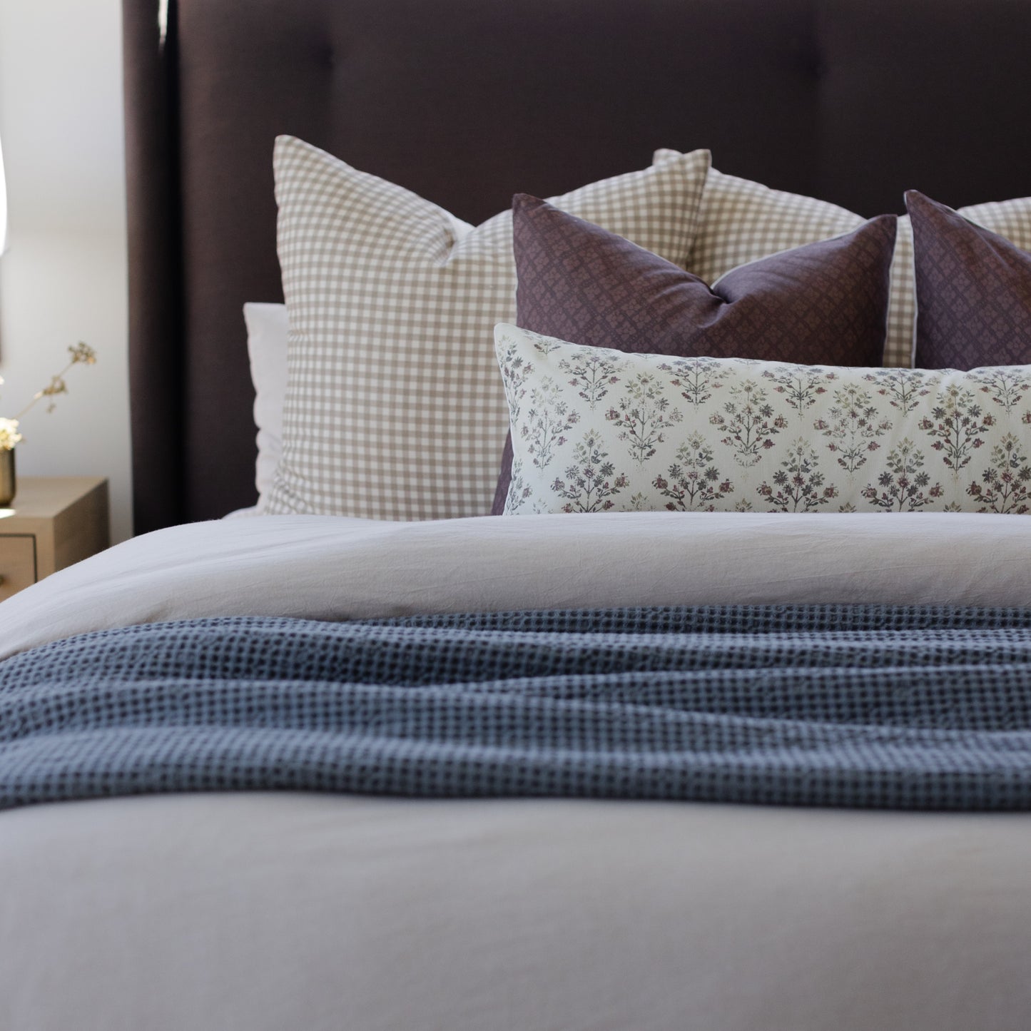 Tan and white gingham pillow displayed among coordinating patterned pillows on a bed.