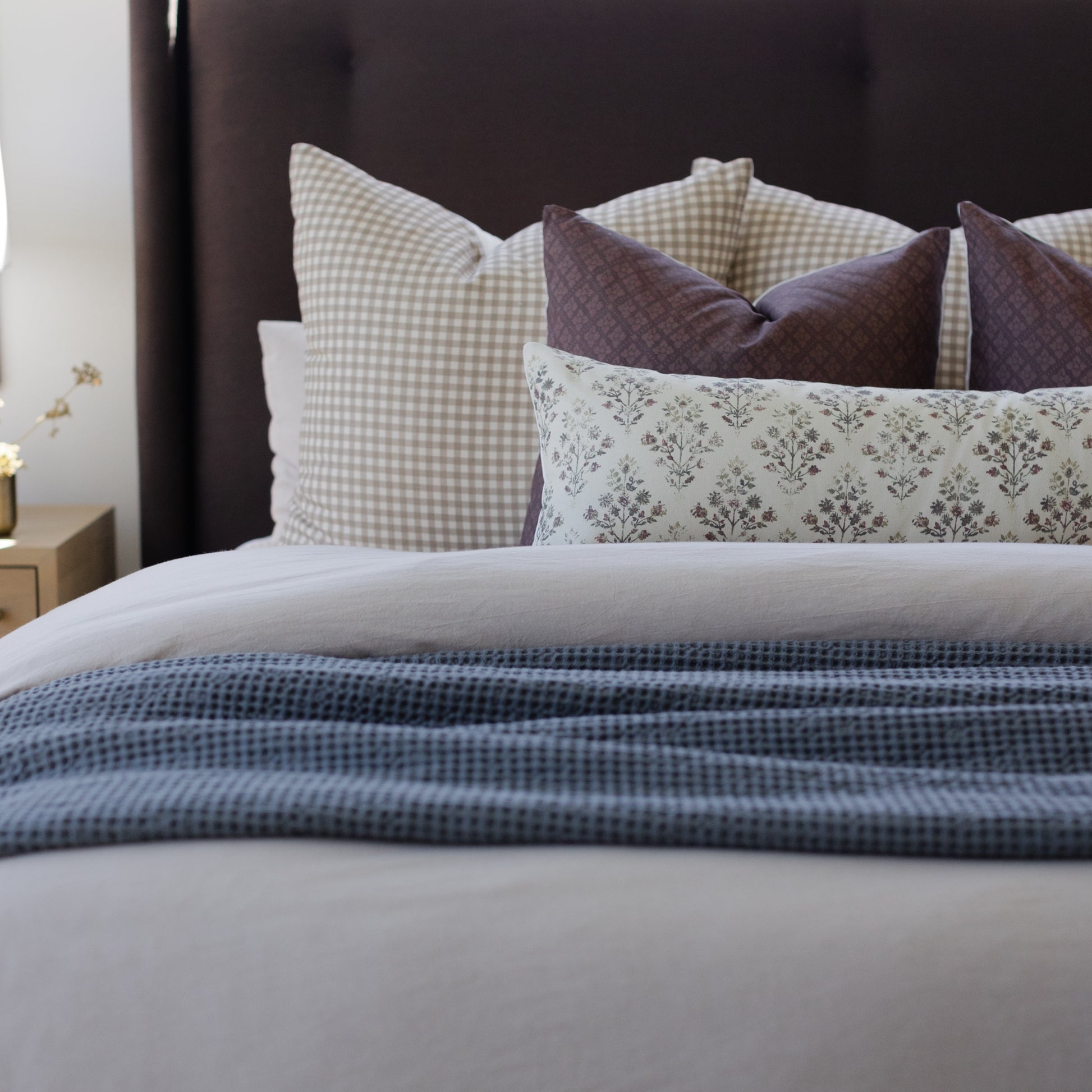 Tan and white gingham pillow displayed among coordinating patterned pillows on a bed.