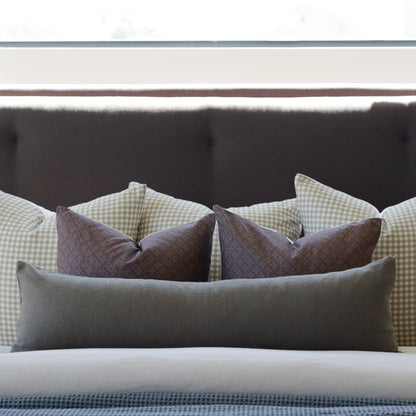 Olive green boucle lumbar pillow displayed on a bed with other decorative pillows and dark headboard.