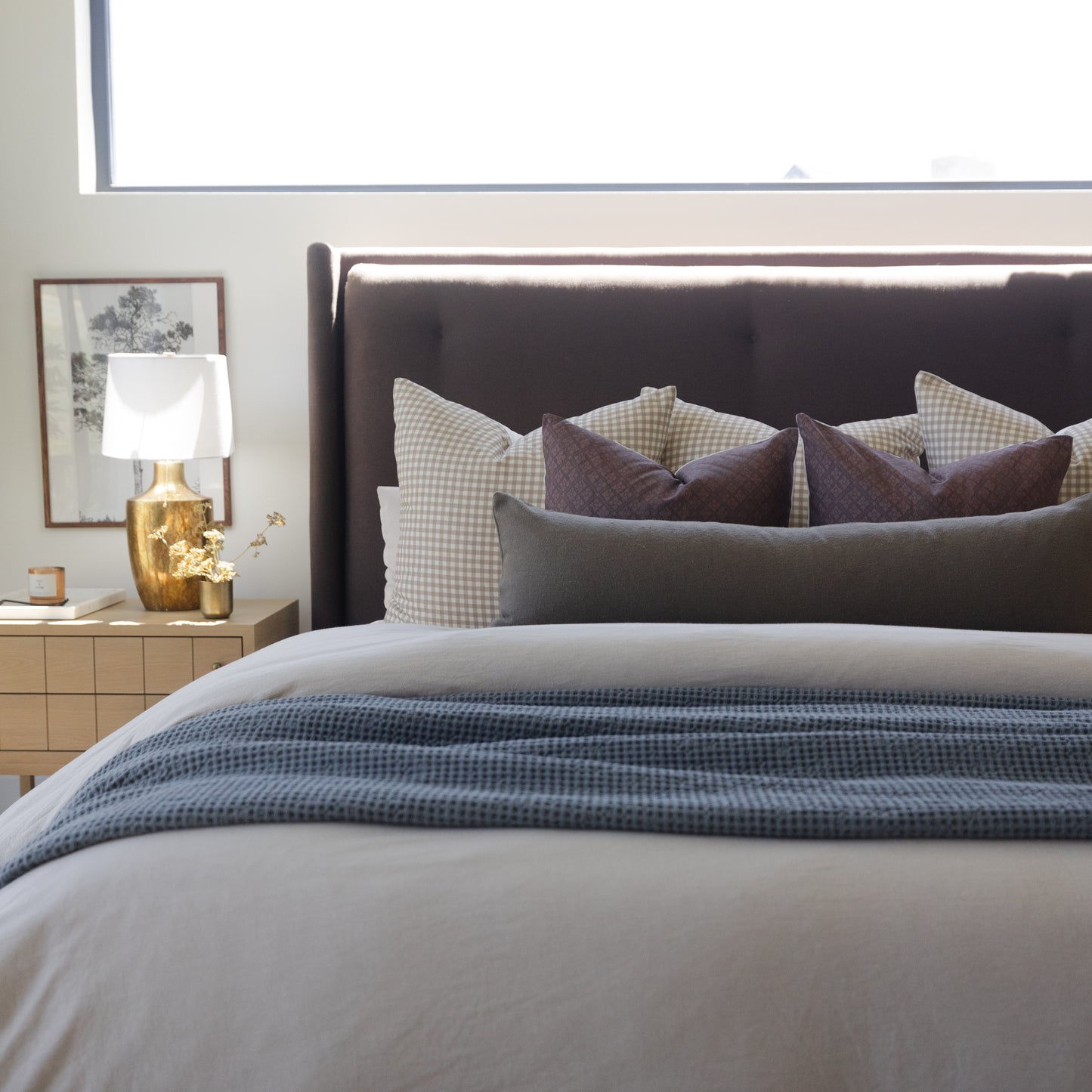 Olive green boucle textured pillows arranged on a bed with checkered and solid accent pillows.