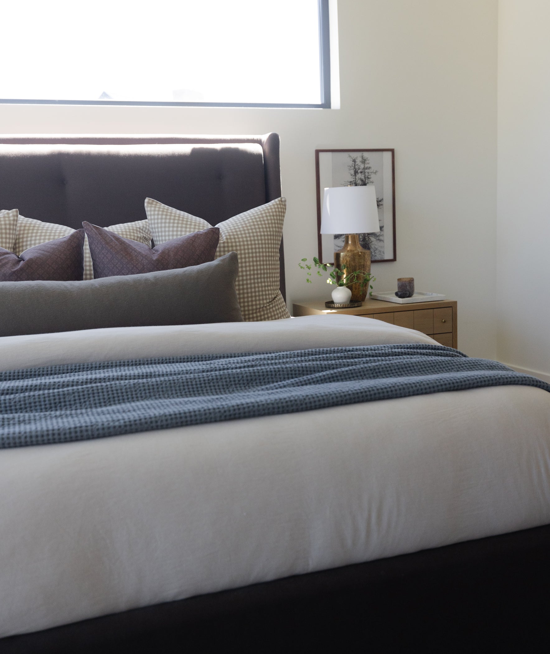 Olive green boucle textured pillow displayed on a bed with gray and checkered cushions.