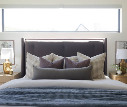 Olive green boucle lumbar pillow displayed on a bed with coordinating pillows and bedding.